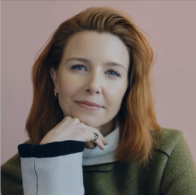 Stacey Dooley smiles to camera with her head in her hand.