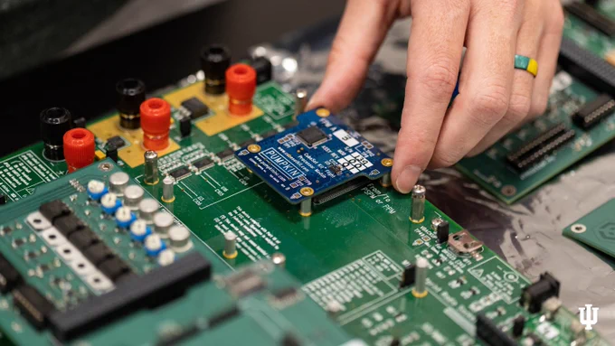 Close-up of a person's hand placing an Arduino microcontroller on a green circuit board, surrounded by various electronic components.