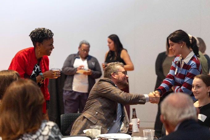 John Green shakes hands with a KU student at a table where others are gathered around for a meal.