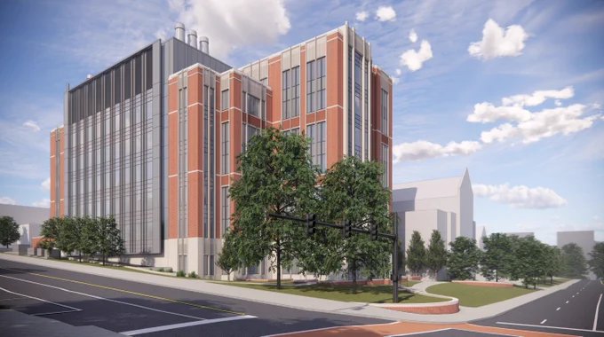 Architectural rendering of a modern multi-story building with red brick and large windows, surrounded by landscaped areas and situated beside a street with parking spaces.
