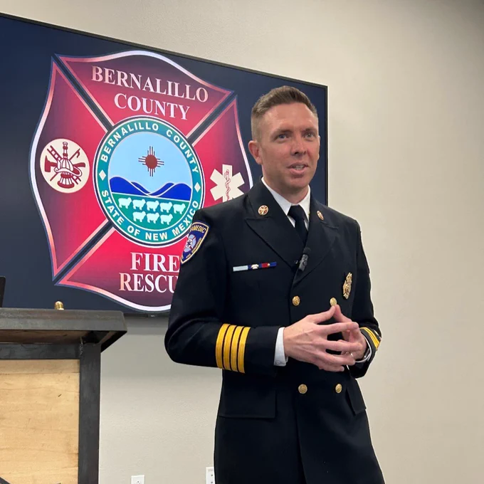 Person in a formal firefighter uniform speaking at a podium with the Bernalillo County Fire Rescue logo in the background.