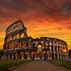 A photo of the Colosseum against an orange sunset sky. 