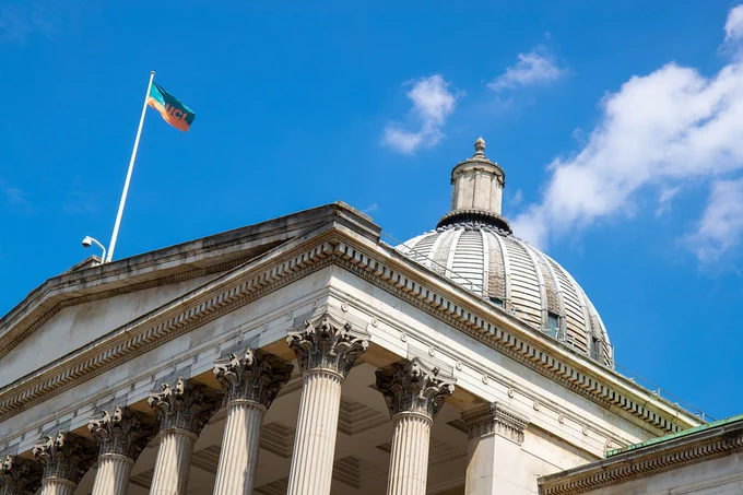 The dome and neoclassical facade of University College London, with its flag waving under a clear blue sky.