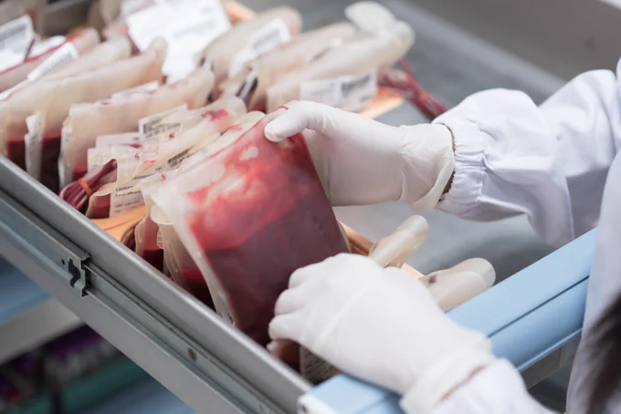 Close up scientist hand holding red blood bag in storage blood refrigerator at blood bank unit laboratory.Doctor selecting fresh donor blood for transfusion.Save life and medical treatment concept.