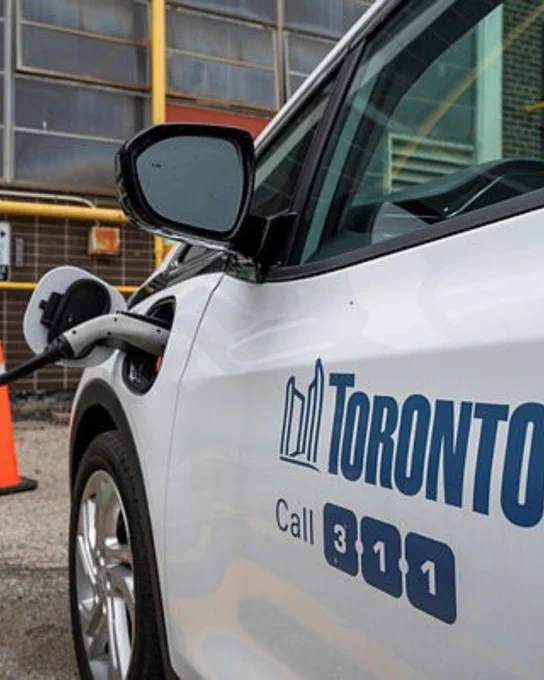 An electric car charging with the City of Toronto logo on the vehicle side. 