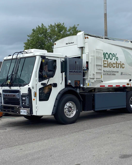 An electric waste collection vehicle with the text "100% Electric" visible on the vehicle side. 