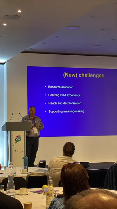 A person standing beside a slide presentation, in front of a seated audience