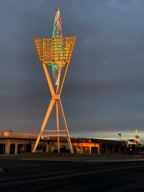 The Odessa Spire is shown illuminated at sunset. Smaller buildings can be seen in the background.