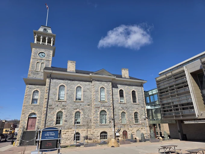 The historic Cambridge City Hall building, made of grey stones with a tall clock tower and blue sky behind.