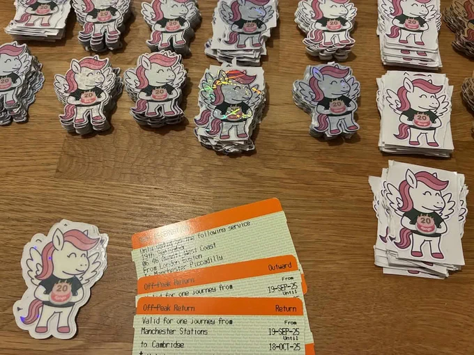Close-up of train tickets on a table, and piles of stickers, with a design of a winged Djangi pony holding a cake