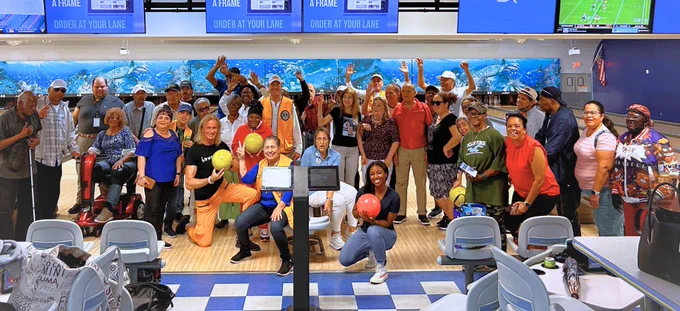 A group photo with 40 people smiling for the camera at a bowling alley.