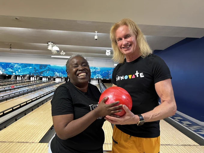 A photo of two people smiling for the camera, holding a bowling ball. Miami Lighthouse Senior Programs participant smiles for the camera with Miami Lighthouse staff Aaron Hill.