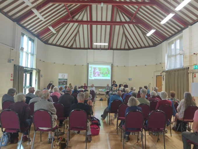 A room full of people listening to a speaker presenting a report