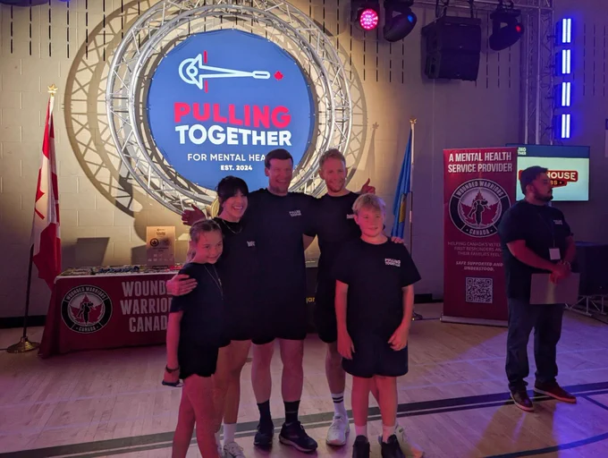 Picture of five people standing in front of a sign lit up that says pulling together for a mental health