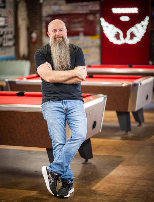 Bryan Kelly smiling and leaning against a pool table.