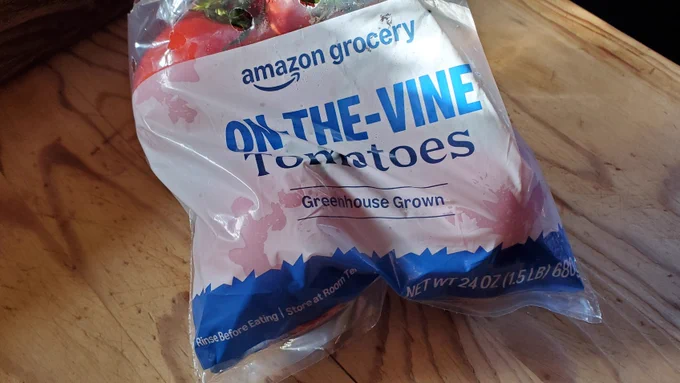 A squashed plastic bag containing Amazon Grocery On-The-Vine Tomatoes that were packed carelessly under a 5 lb. bag of potatoes by an idiot employed by Amazon Prime's same-day grocery delivery service.
