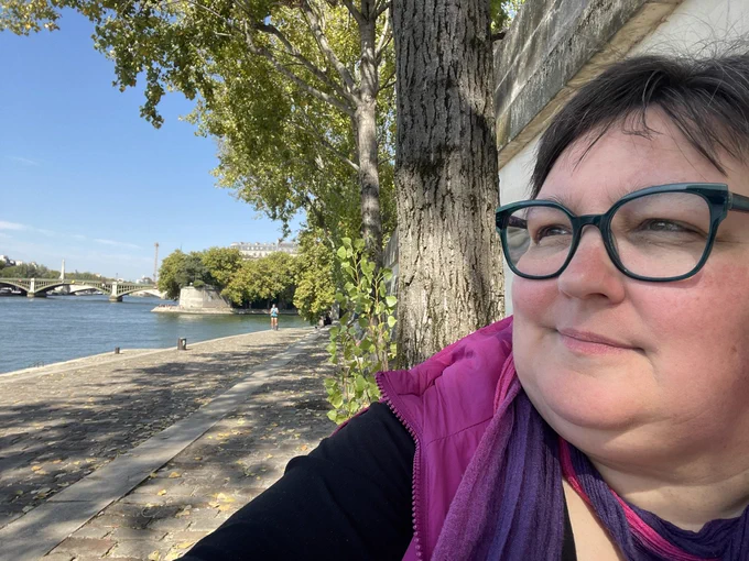 middle-aged woman wearing glasses looking onto the water of a river nearby
