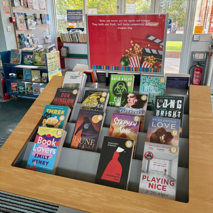 A red poster on top of a display pod at Ash Library, with a quote on a red background reading: 'Books and movies are like apples and oranges. They both are fruit, but taste completely different' by Stephen King. Underneath are four rows of books, all of which have been adapted into films.