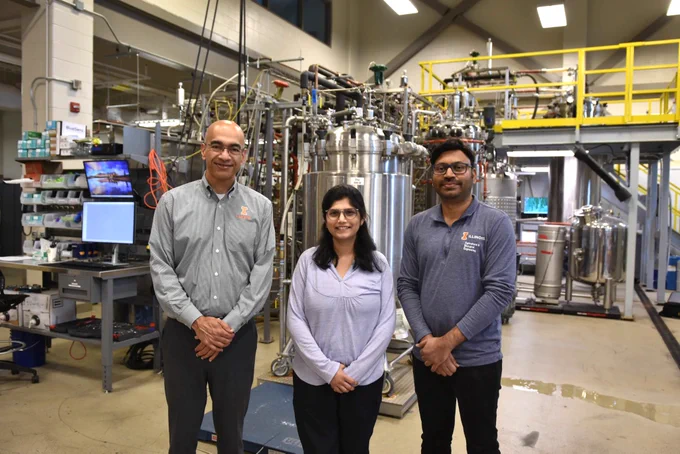 A photo of three researchers standing in front of bioprocessing equipment at the Integrated Bioprocessing Research Lab at the University of Illinois Urbana-Champaign