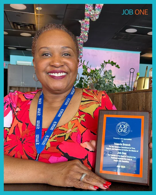 Yolanda wearing a red shirt holding a plaque celebrating her time as a board member.