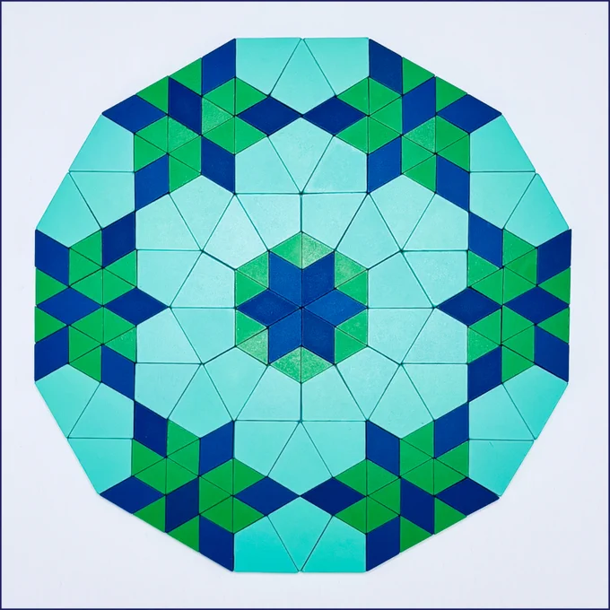 The image shows a twelve-sided shape created with 21st Century Pattern Blocks. It was built by arranging 6 rectangles and 6 equilateral triangles around a central regular hexagon with each side of the hexagon measuring 2*sqrt(3) inches. The design uses blue rhombuses, green triangles, and teal kites.
