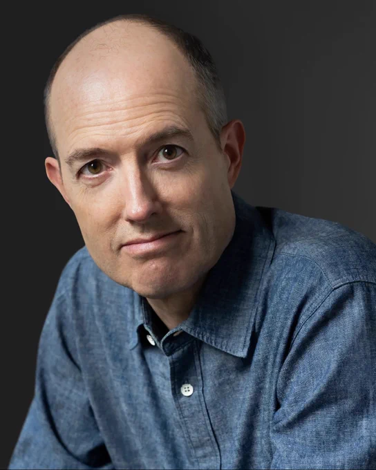 Portrait of a person wearing a denim shirt against a gray background.