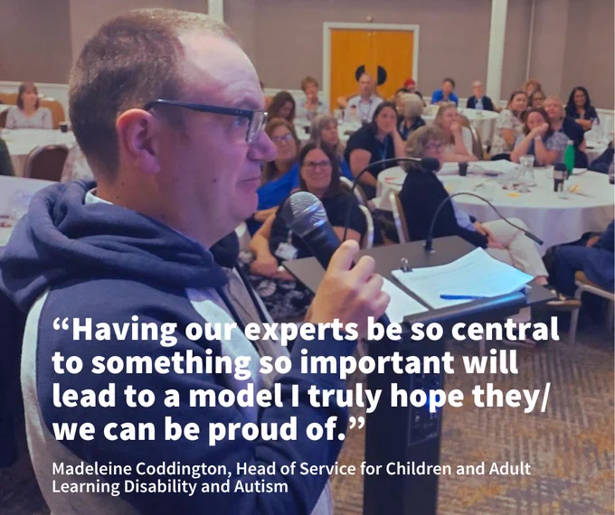 Speak Out Leader Sean speaking into a microphone at a podium in front of an attentive audience seated at round tables in a conference room. A quote is layered over the top which talks about the benefits of co-production.