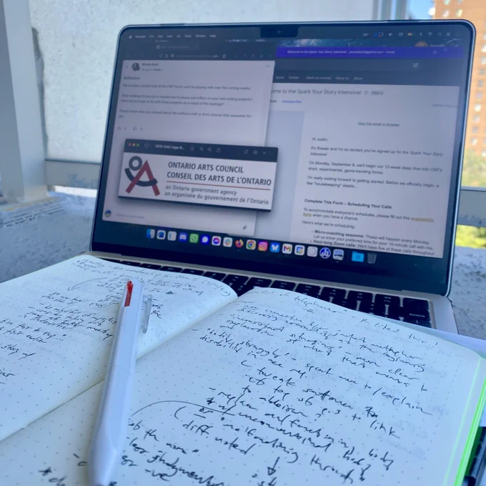 A picture of a laptop computer with several browser windows open, one of which displaying the Ontario Arts Council logo. Across the laptop keyboard is an open notebook displaying handwritten notes, with a pen on top.