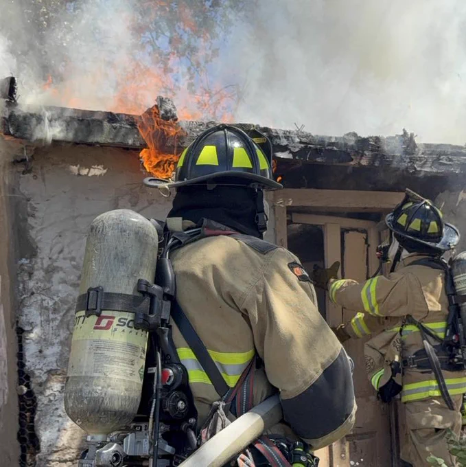 Firefighters wearing full gear extinguish flames in a burning building.