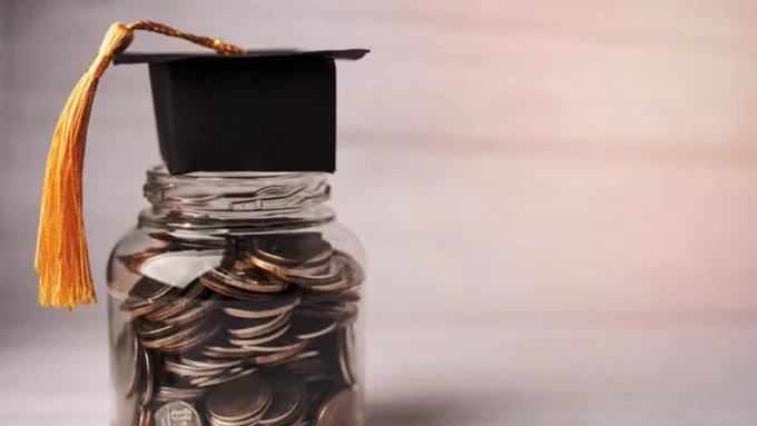 A jar full of coins with a graduation cap complete with tassel on top.