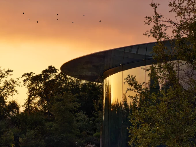 A photo of Steve Jobs Theater at sunrise, with birds flying in the sky in the background.