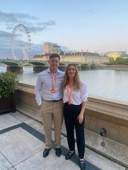 A man and a woman standing on the terrace of the Houses of Parliament.