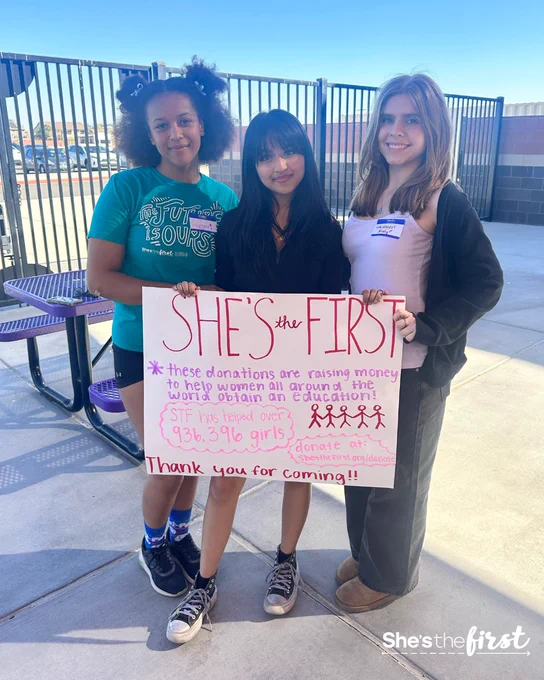 Photo of Siyaa (middle) and 2 fellow chapter members holding a She's the First sign.