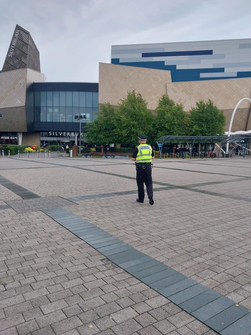 Officer walking near to bus station at Silverburn with shopping centre entrance in foreground