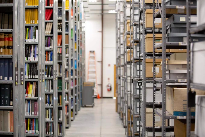 [ID: Pictured is a photo of several bookshelves in the Library Collection Depository.]