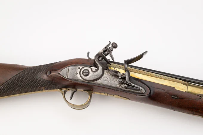 A historic flintlock musket with a wooden stock, brass fittings, and metal firing mechanism, photographed on a plain white background.