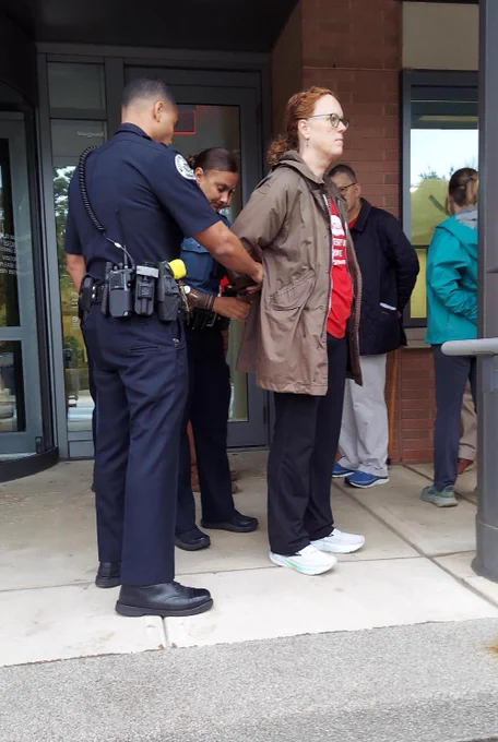 [Alt text: A few people getting arrested by police officers in front of an office building. Photo by Lee Smithey]