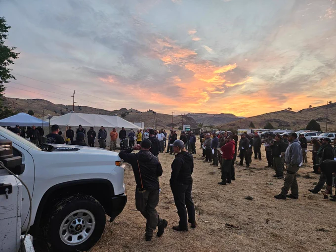 A group of firefighters at an outdoor meeting with tents and vehicles all around.