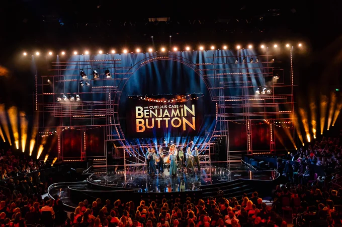 Stage view of a live performance from The Curious Case Of Benjamin Button, featuring multiple performers and vibrant lighting with a prominent backdrop at the Olivier Awards
