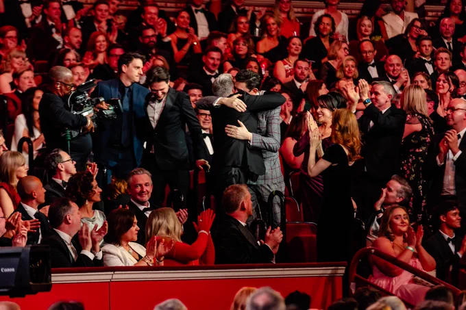 Attendees at the Olivier Awards applauding enthusiastically as one individual hugs another on stage.