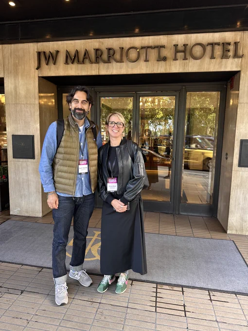 A man and a woman stand in front of the JW Marriott Hotel entrance, smiling for a photo.