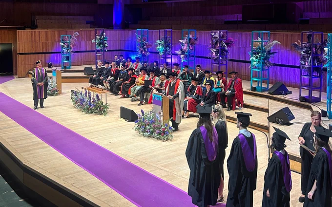 Graduation ceremony at the Southbank Centre auditorium, with students walking across the stage to receive their diplomas while faculty members, dressed in academic regalia, observe from their seats.