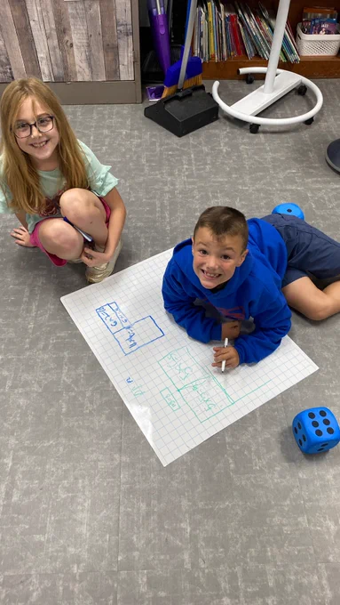 boy and a girl sit on the floor and use a marker to write on giant graph paper during a third grade math lesson