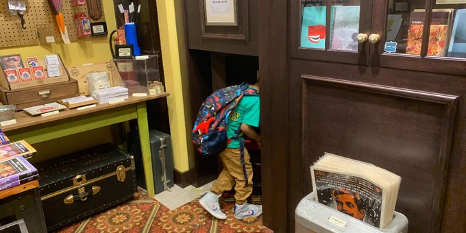 A student wearing a backpack walks through the hidden door in Tivoli's Astounding Magic Supply Co.