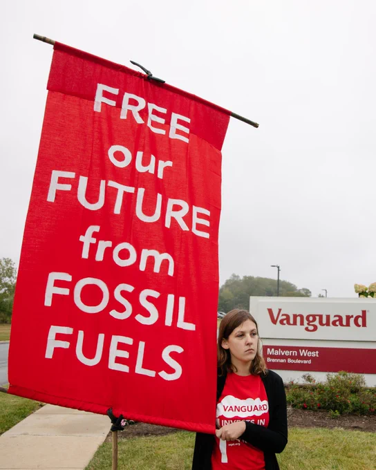 A person sustains a large red banner with white text that says “free our future from fossil fuels” in front of a sign that says “Vanguard.” Photo by Rachael Warriner