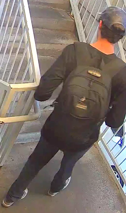 Person wearing a black backpack and cap walking up concrete stairs enclosed by metal railings and gates.