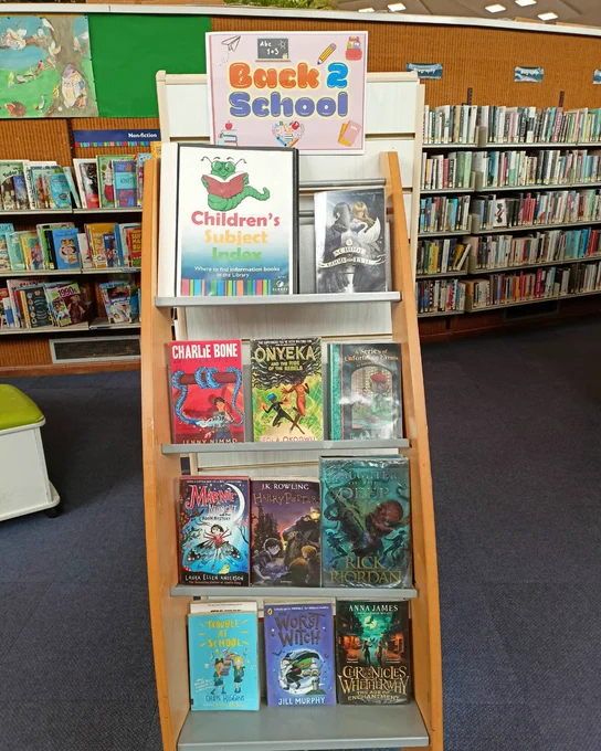 Photograph of a tall wooden book display with tiered shelves. A poster at the top of the shelf reads "Back2School". Books on the display include The School for Good and Evil by Soman Chainani, Charlie Bone and the Blue Boa by Jenny Nimmo, The Austere Academy by Lemony Snicket, Harry Potter and the Philosopher's Stone by J.K. Rowling, and The Worst Witch by Jill Murphy. 