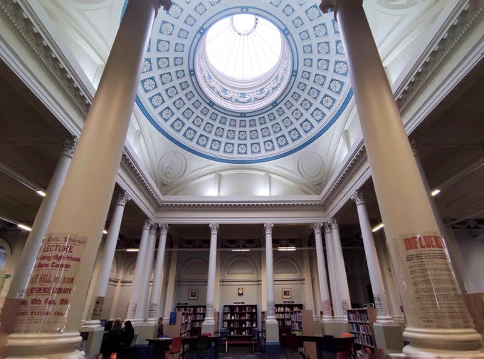 Interior of Belfast central library with tall white columns and a large ornate blue and white domed skylight ceiling.