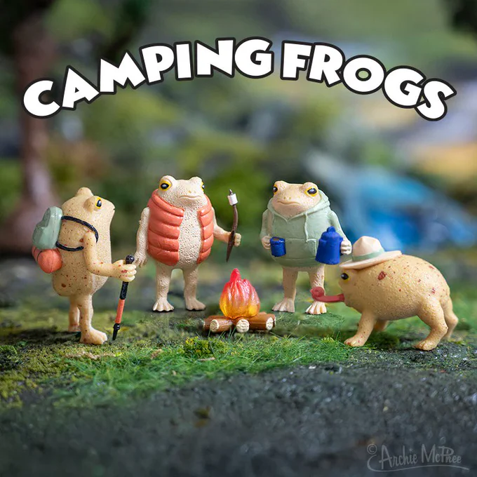 Four rain frog figurines dressed in camping gear, gathered around a small campfire. The frogs are holding various camping items, such as a walking stick and mugs, with a natural backdrop. The text says, "CAMPING FROGS