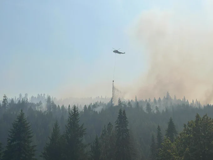 Fire helicopter drops water from a bucket on a burning section of forest.